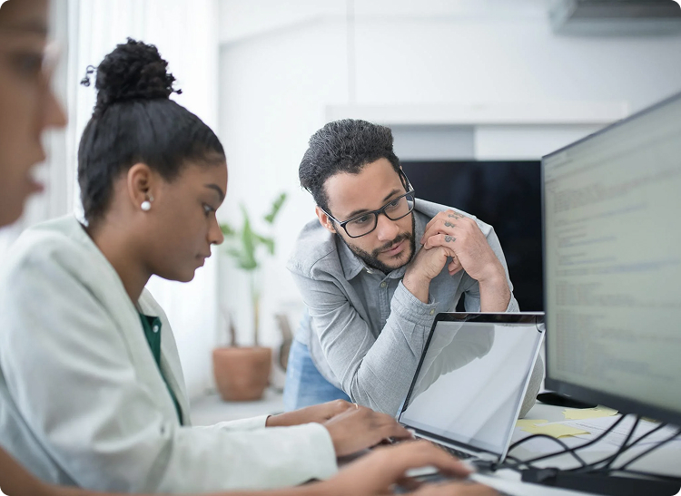 Two people collaborating at a desk with a laptop and a large monitor.