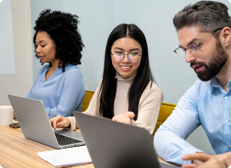 Three colleagues working at laptops, with one woman smiling and gesturing during discussion.